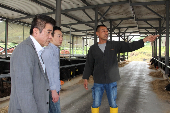 「椚座牛」の生産地を訪れ、生産者(右)から肥育方法について説明を受ける田中総料理長(左)