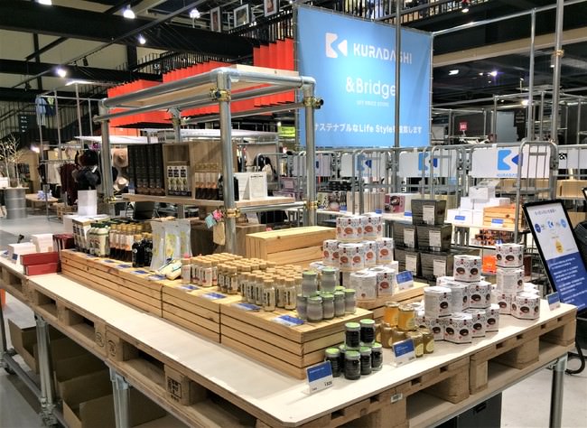 「アンドブリッジ」の最大店舗 ひたちなか店頭 （茨城県ひたちなか市新光町35番地） 1階入ってすぐに設置した「KURADASHI」コーナーには食品、お菓子、飲料、調味料その他化粧品までが並ぶ